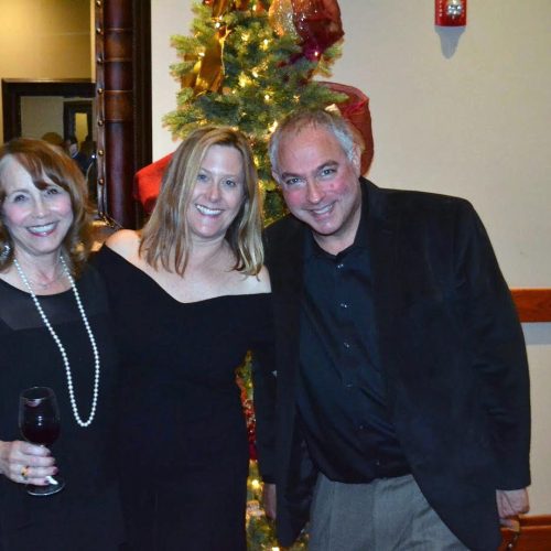 Two woman and a man in front of a Christmas tree