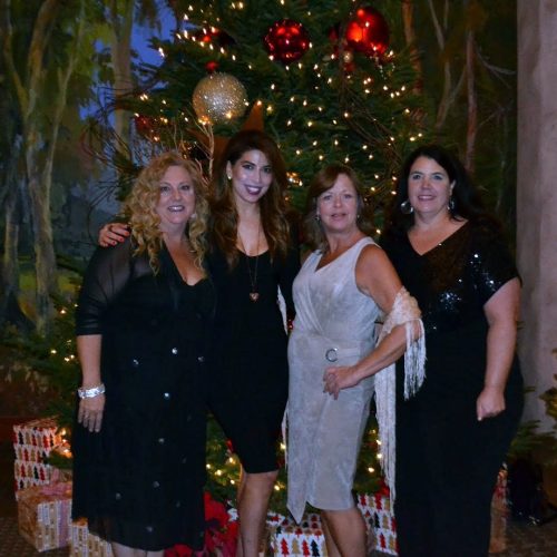 Three women posing in front of a Christmas tree